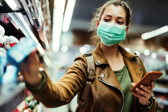 A young woman with a face mask is buying a product in a store. It demonstrate a customer experience of buying during the covid-19.