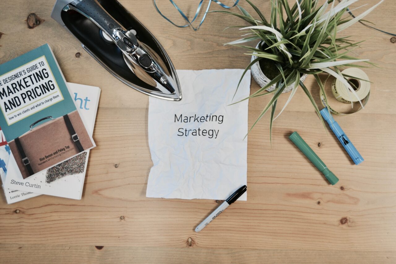 A desk of a digital marketer with books, pens, and a paper containing digital strategy.