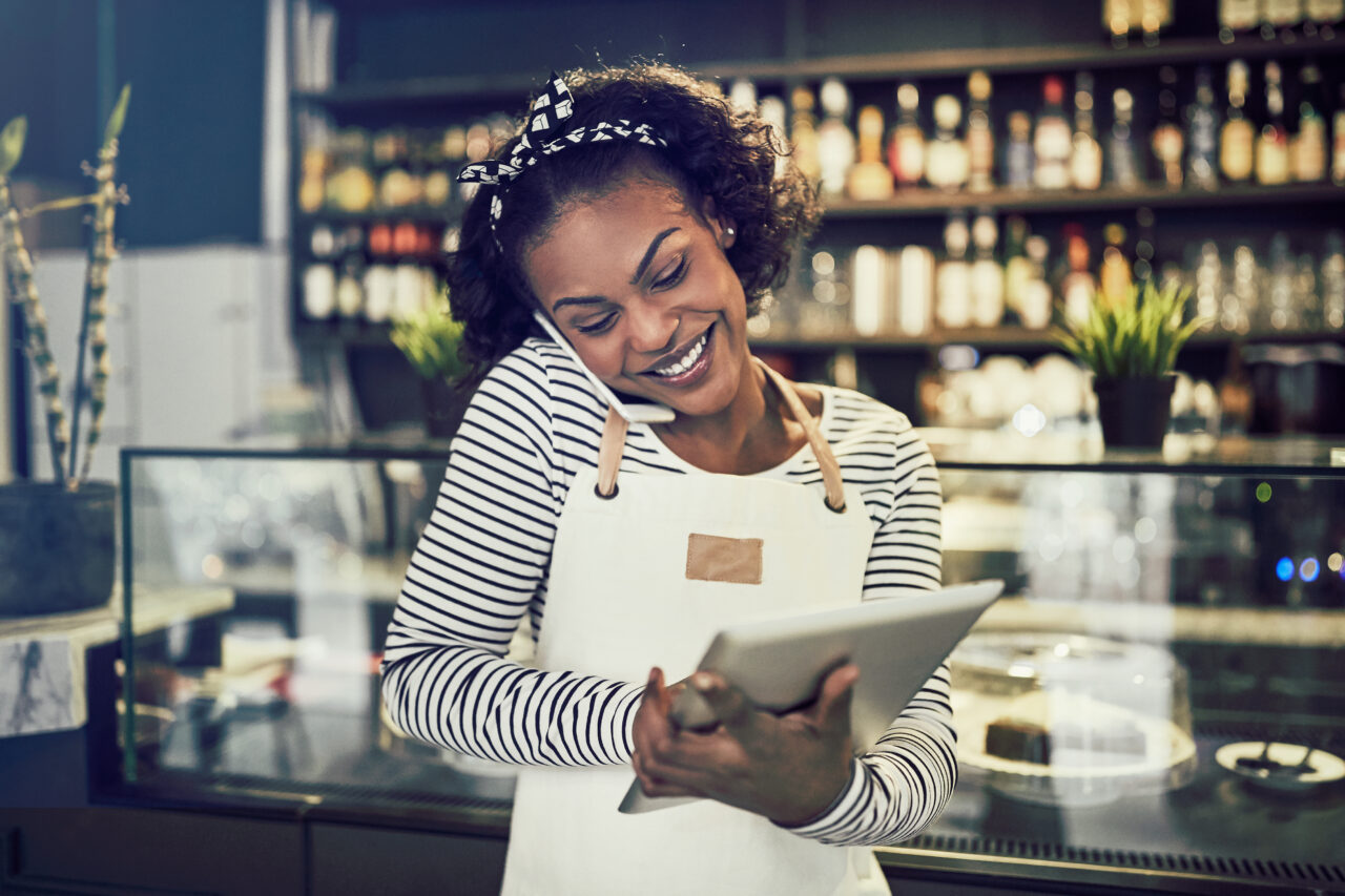 A woman talks on her phone and uses her laptop to talk with her employer about how small businesses can compete with big brands.