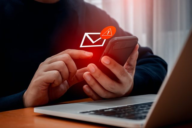 SMS spam, fake text message phishing from scammer concept. System hacked red warning alert, email hack, scam malware spreading virus on message alert virtual on mobile phone screen in person hand.