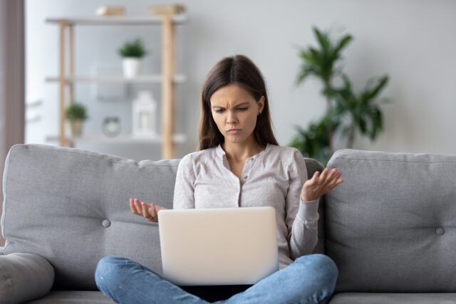 Annoyed woman using laptop, sitting at home.