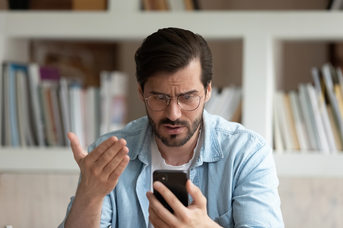The image shows an unhappy man with an app on his phone.